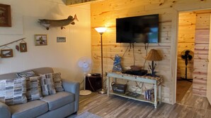 Una sala de estar acogedora con un sofá, televisor, ventilador y una pared de madera.