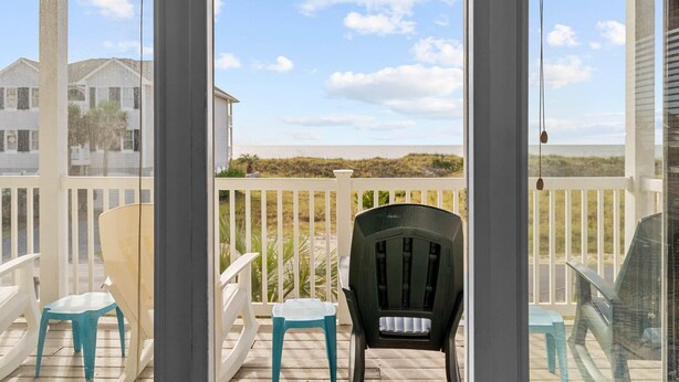 A covered outdoor area with a view of the beach, featuring a wooden deck, white railings, and two chairs. - CottageVacations4u "Ocean Paradise" -Ocean views! -pool club-dog friendly- elevator (Ocean Isle Beach)