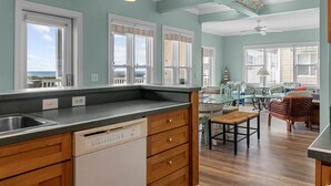 A kitchen with a dishwasher, wooden cabinets, and a dining area with wicker furniture. - CottageVacations4u "Ocean Paradise" -Ocean views! -pool club-dog friendly- elevator (Ocean Isle Beach)