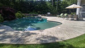 A swimming pool with a stone border, a grill, and outdoor seating.