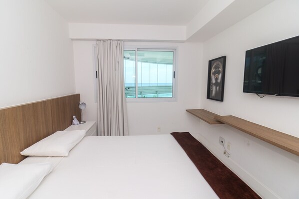 A modern hotel room with a large bed, a TV mounted on the wall, and a window with a view of the sea. - Pontal Beach Ocean View (Rio de Janeiro)