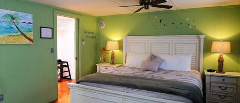 A bedroom with a bed, two bedside tables with lamps, a ceiling fan, a door, and a wall with a painting.