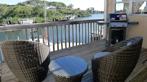 Un balcon doté de meubles en osier, d’un barbecue et offrant une vue sur une marina avec des bateaux et de la verdure.