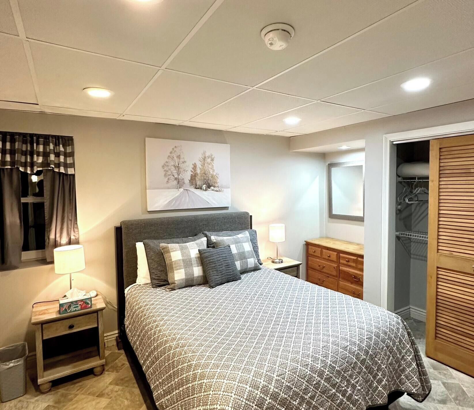 A bedroom with a bed, nightstands, a dresser, a closet, and a painting on the wall.
