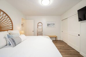 Un dormitorio con cama, mesita de noche, lámpara y una puerta con perchero para toallas.