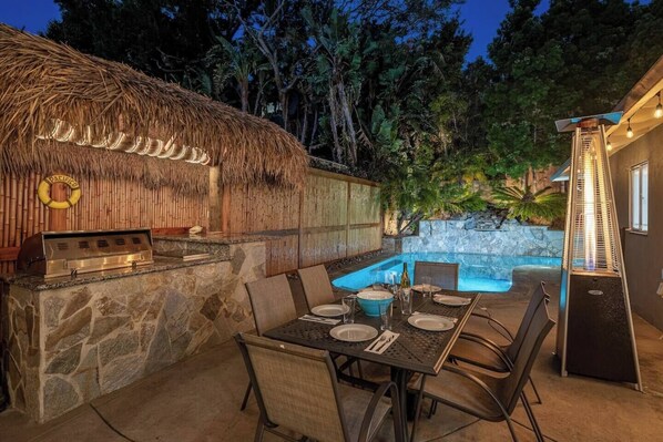 Un espacio de comedor al aire libre con pared de piedra, una parrilla y una piscina.