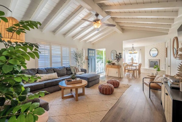 A spacious living area with a high ceiling, a sofa, a coffee table, and a dining area with chairs and a table.