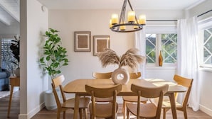 Un'area pranzo con un tavolo rotondo in legno, sei sedie, un lampadario e quadri appesi al muro.