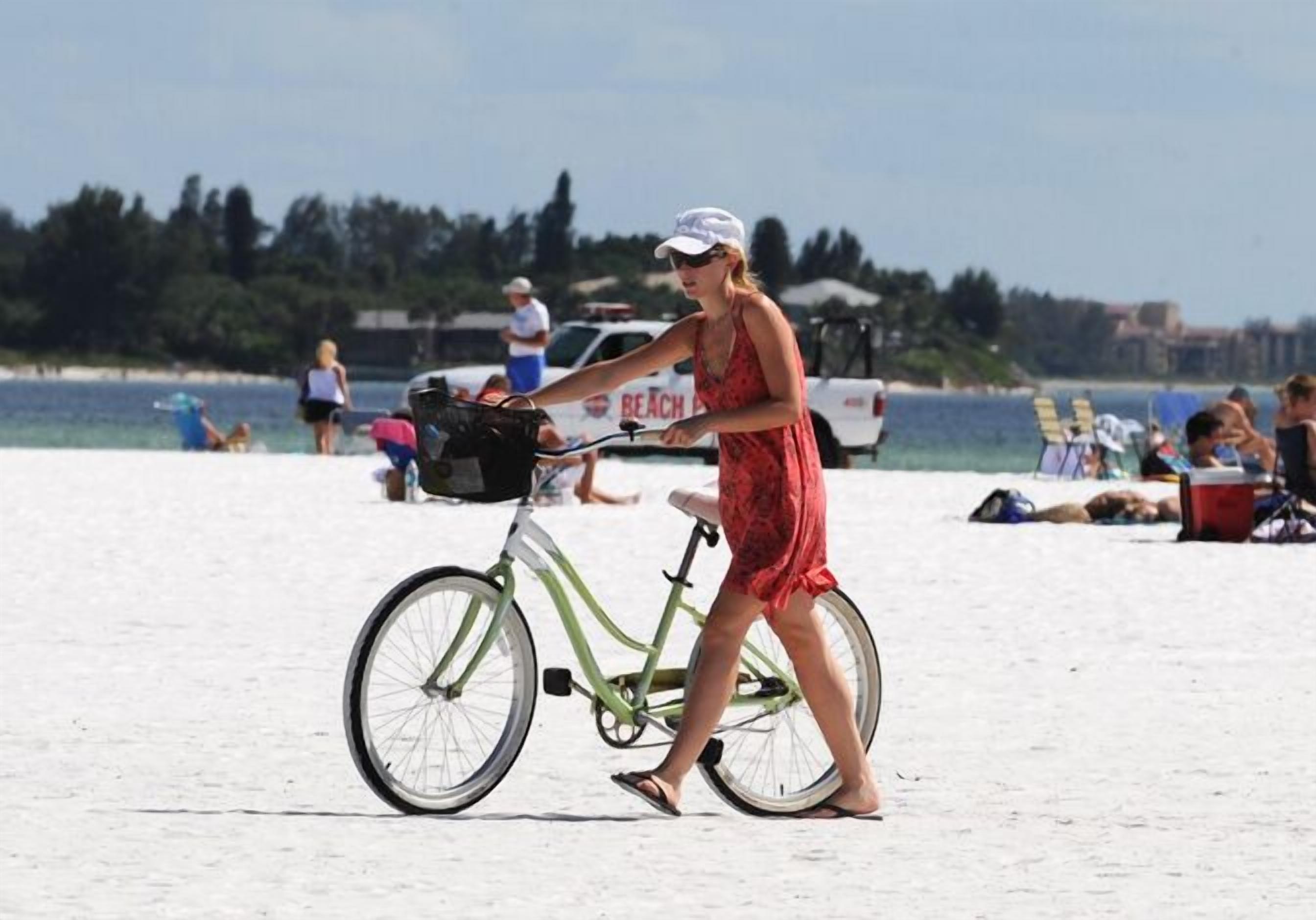 En person cyklar på en sandstrand, och i bakgrunden syns ett fordon med texten ”BEACH” på.