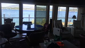 A room with a large window overlooking a lake, a dining table, and several chairs.