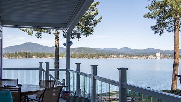 A covered outdoor area with a table and chairs, overlooking a calm lake with mountains in the background.