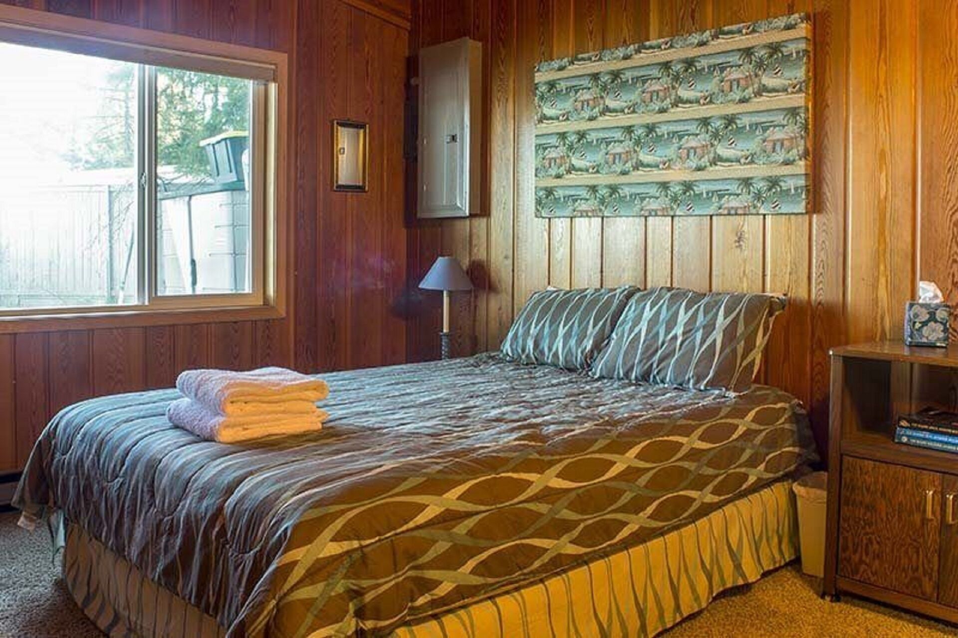 Ein Schlafzimmer mit Bett, Fenster, Lampe und einer Wand mit tropischem Wandbild.