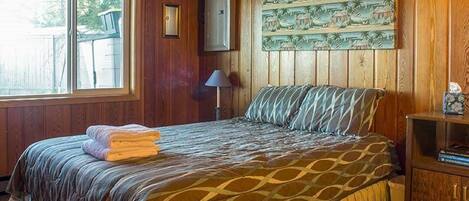 Ein Schlafzimmer mit Bett, Fenster, Lampe und einer Wand mit tropischem Wandbild.