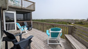 Una terraza de madera con dos sillas Adirondack y un banco, con vista a un paisaje costero.