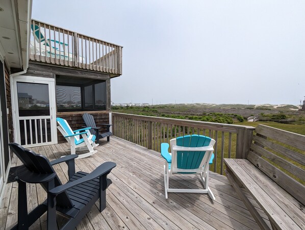 Una terraza de madera con dos sillas Adirondack y un banco, con vista a un paisaje costero.