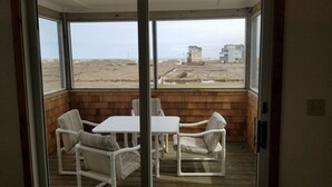Un balcón con sillas y una mesa blancos, con vista a una playa y edificios.