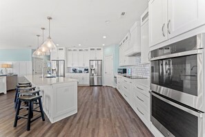 Una cocina moderna con armarios blancos, electrodomésticos de acero inoxidable y una isla central con taburetes.