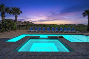 Una piscina con una fuente de agua cristalina azul, rodeada de sillones de descanso y palmeras.