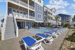 A poolside area with lounge chairs and a staircase leading to a building with multiple balconies. - Enjoy a Luxurious Vacation at Ocean Blue - 8 Bed/8.5 Bath Home with Pool & Hot Tub (North Myrtle Beach)