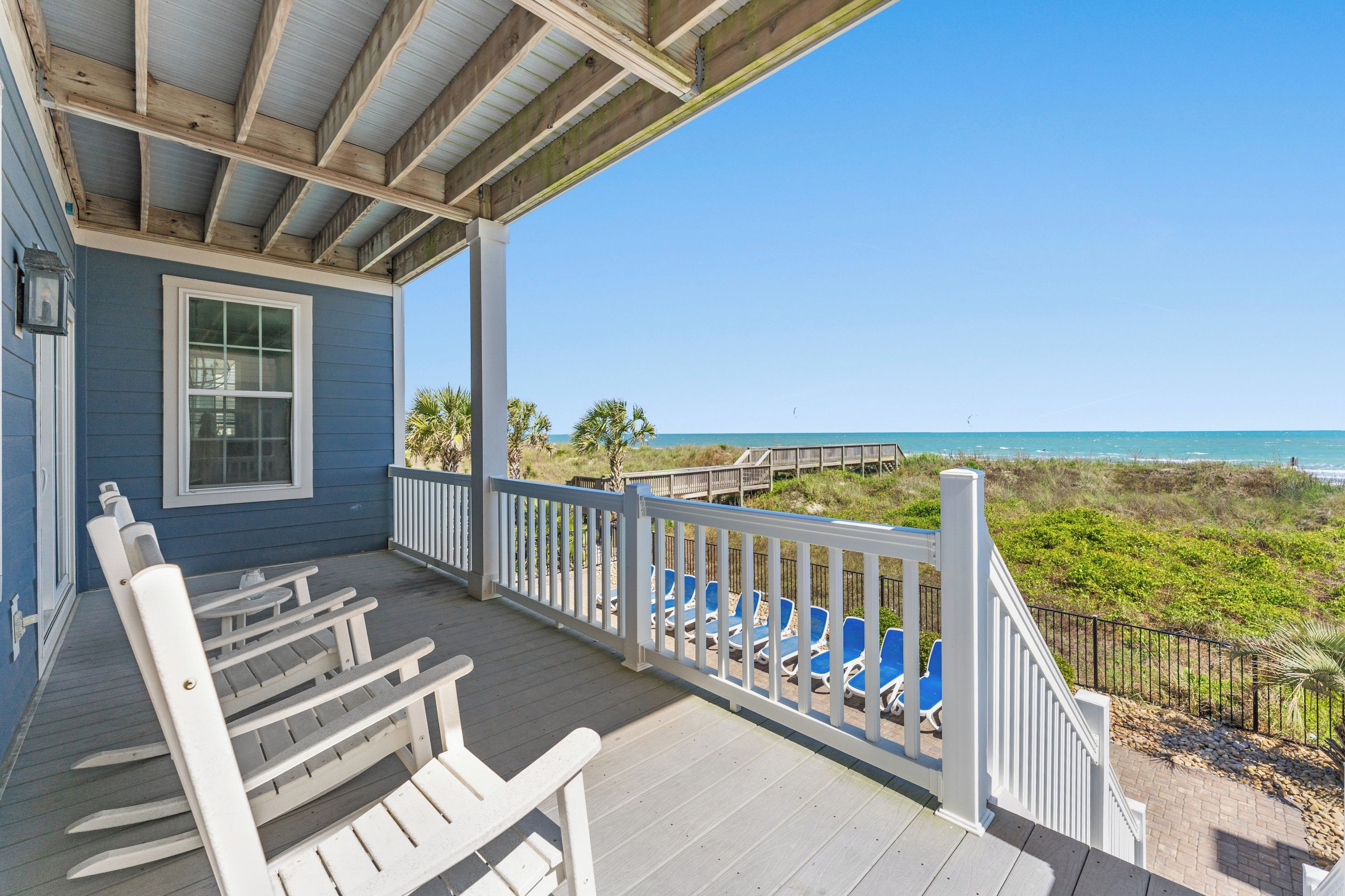 A covered porch with white railings, a view of the beach, and a wooden deck.