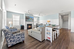 A spacious living room with a fireplace, a dining area, and a kitchen with a view of the outdoors.