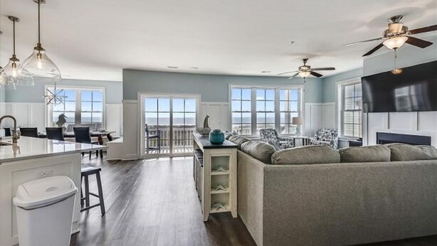 A spacious kitchen with a central island, a dining area with a view, a living room with a sofa, and a ceiling fan.