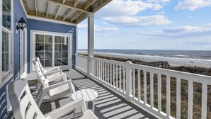 A covered porch with white railings, a view of the beach, and a door with glass panels.