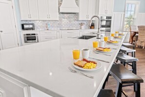 Cocina moderna con armarios blancos, una isla grande y espacio para desayuno con tostadas, huevos y jugo.