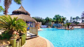 A swimming pool with a thatched-roof structure, palm trees, and a paved walkway. - Slow Mo 17AD-Beautiful Beach Cottage @ the Purple Parrot Resort/Perdido Key FL (Pensacola)