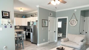 A modern kitchen with white cabinets, stainless steel appliances, and a dining area with a wooden table and chairs. - Slow Mo 17AD-Beautiful Beach Cottage @ the Purple Parrot Resort/Perdido Key FL (Pensacola)