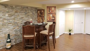 A dining area with a stone wall, wooden chairs, a glass-top table, and a wine bottle.