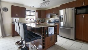 A modern kitchen with wooden cabinets, stainless steel appliances, and a bar area with stools.