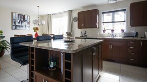 A modern kitchen with a central island, wooden cabinets, and a dining area with a black sofa and a table.