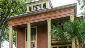 A two-story house with a porch, a flag, and a picket fence. - Beautiful Home in Historic Neighborhood
1/2 mile to Downtown and the Riverwalk (san antonio)