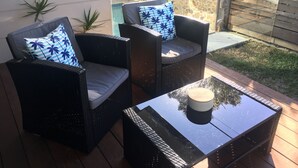 Two wicker chairs with blue and white patterned cushions, a black table with a wooden top, and a stone wall in the background. - Husky Getaway - Villa with Heated Plunge Pool (Huskisson)
