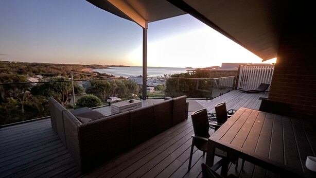 Terraza con mobiliario exterior, con vistas a un paisaje costero al atardecer.