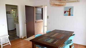 Un comedor con una mesa de madera y sillas azules, un refrigerador blanco y una puerta que da a una cocina.