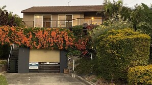 Un edificio de dos plantas con una puerta de garaje, rodeado de exuberante vegetación y plantas con flores.