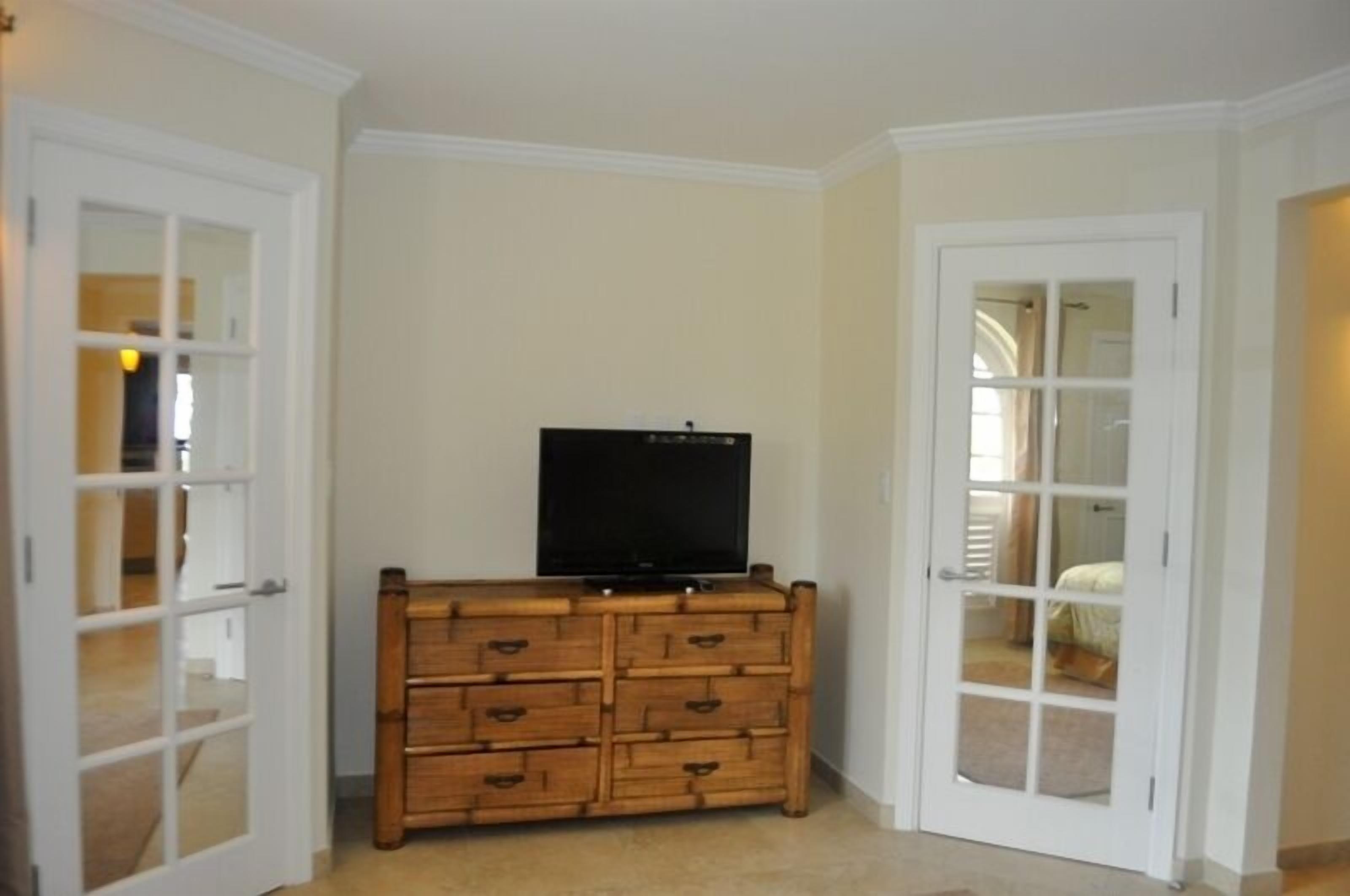 Una habitación con un aparador de madera, un televisor encima y una puerta que da a otra habitación.