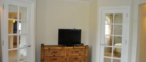Una habitación con un aparador de madera, un televisor encima y una puerta que da a otra habitación.