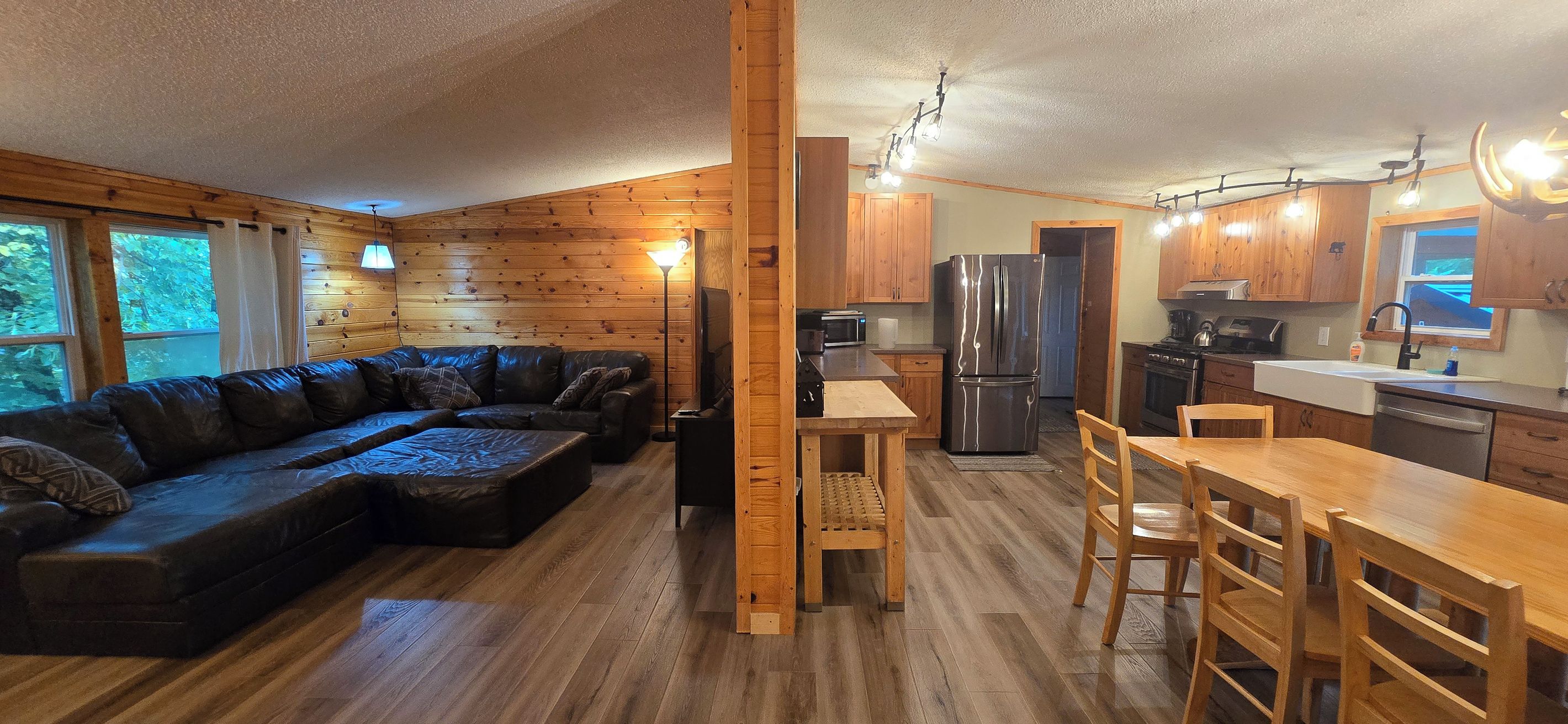 Interior d'una cabana amb elements de fusta, un sofà, una taula de menjador i una zona de cuina.