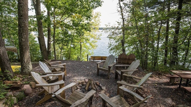 Un camping junto al lago con sillas Adirondack de madera dispuestas alrededor de un brasero central, rodeado de árboles y vistas al lago.