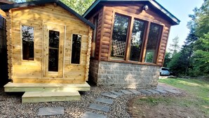 Dos cabañas de madera con ventanas grandes, un sendero de piedra y un coche aparcado cerca.