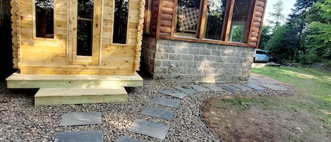Two wooden cabins with large windows, a stone pathway leading to them, and a car parked nearby.