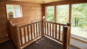 Interior de una cabaña de madera con barandilla de madera, una ventana pequeña y vistas a la vegetación exterior.