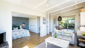 Un salon moderne avec un canapé, une table basse et un téléviseur. On aperçoit, au fond, un lit recouvert d’une couvre-lit à motifs.