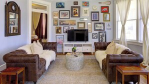 Un salon avec deux canapés en cuir, un téléviseur et un mur décoré de divers tableaux encadrés.