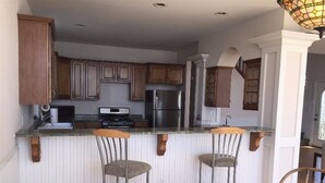 Una cocina con armarios de madera, un refrigerador de acero inoxidable, un horno empotrado y una barra con dos taburetes.