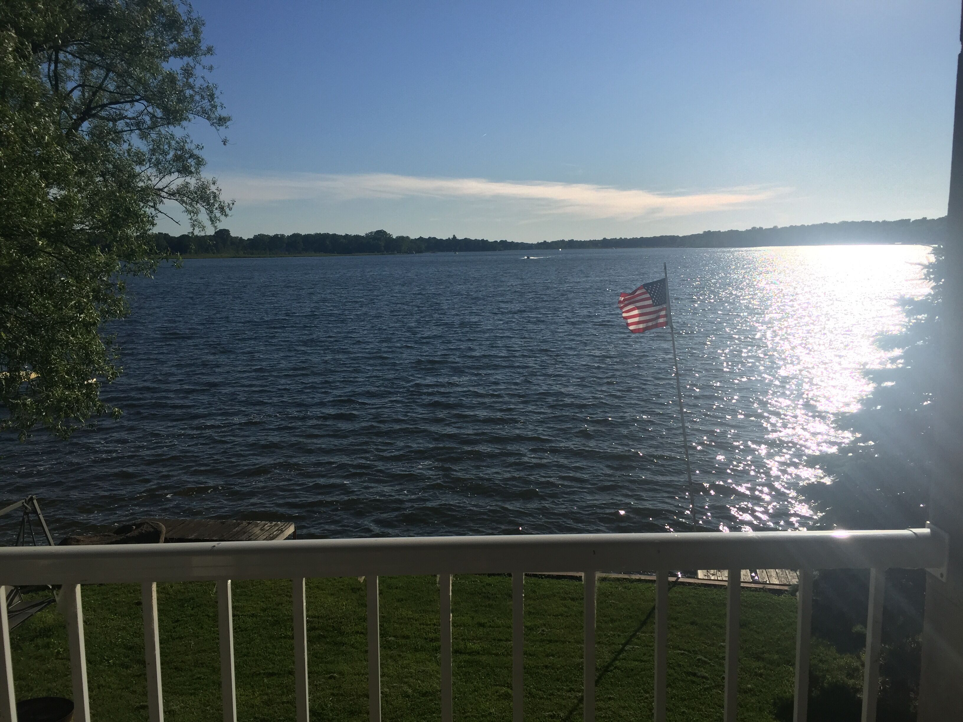 Vista de un lago con una bandera estadounidense en un asta, un área cubierta de césped y una barandilla.
