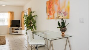 Een moderne woonkamer met een glazen eettafel, een witte leren bank, een potplant en een flatscreen televisie op een witte kast.